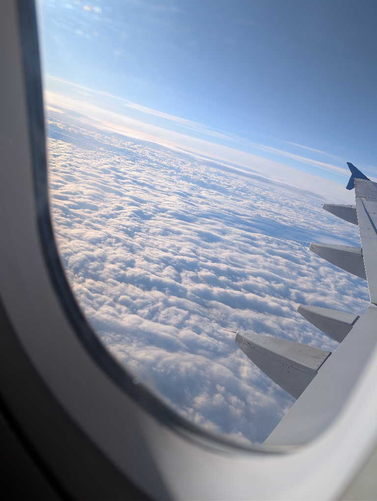 This picture shows a view looking down at the clouds from an airplane window.