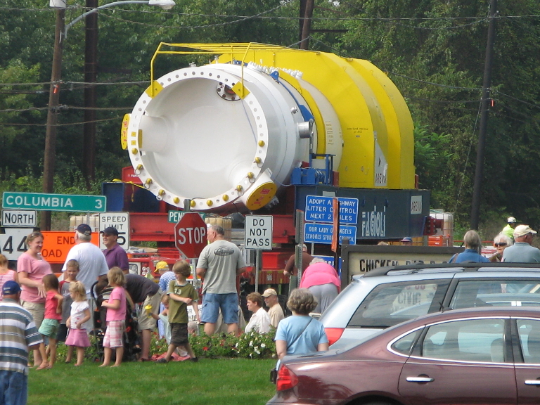 This picture a very large generator being moved up a road.