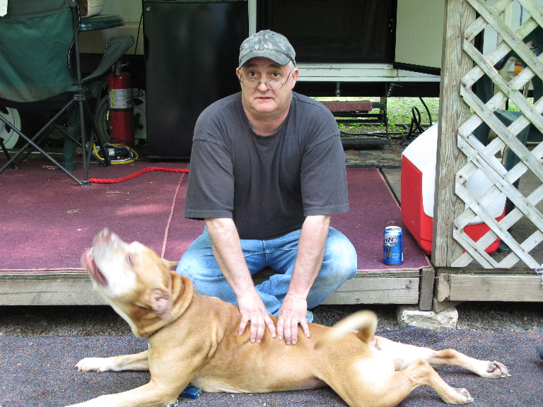 This is a picture of my brother's reddish pitbull, reds. He's laying on a porch with my dad petting him.