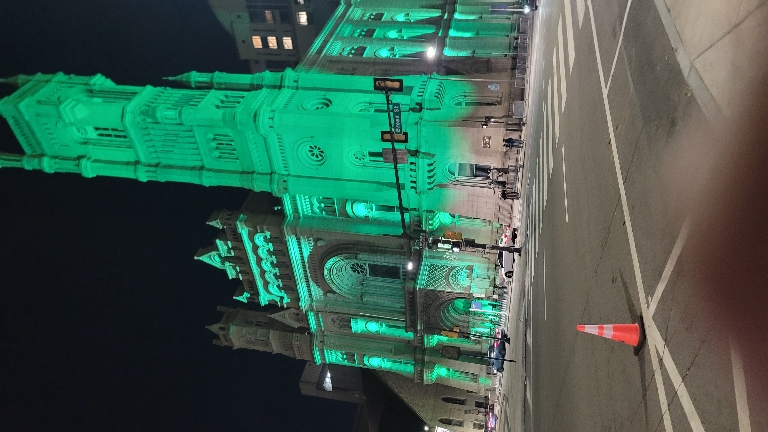 This picture shows the large church Near City hall lit up by green lights at night.