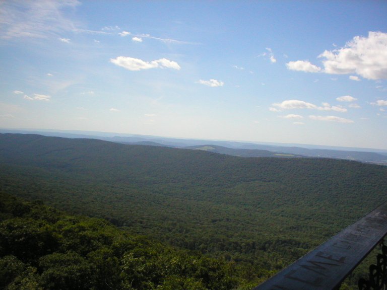 This picture from the fire tower shows a somewhat hazy view of mountains. There a few clouds in the hazy skies.
