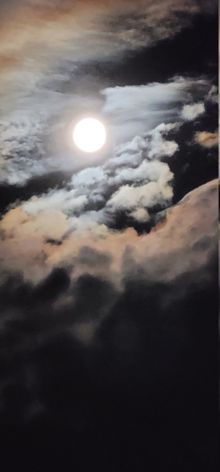 This picture shows the full moon with brightly lit clouds around it.