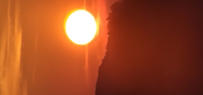 This picture the sun near the horizon. The sun is very orange along with the sky around it.