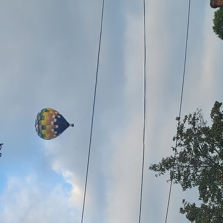 This picture shows a multicolored hot air balloon the the sky with clouds above it.