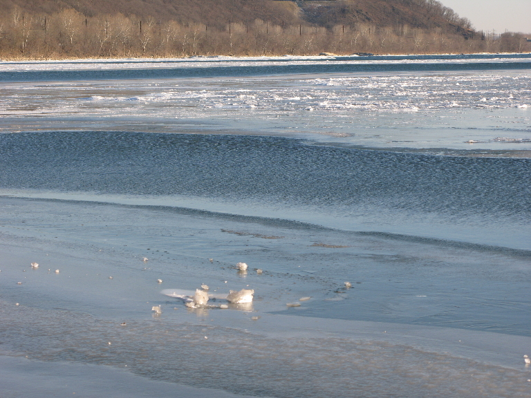 This photo shows a couple of blocks of ice on top of the sheet ice on the river.