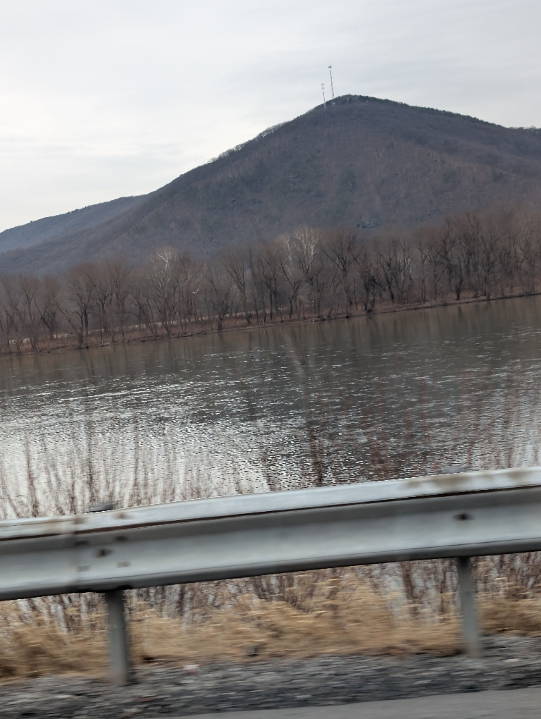 This picture shows a view out a car window of the Susquehanna River with a mountain across it.