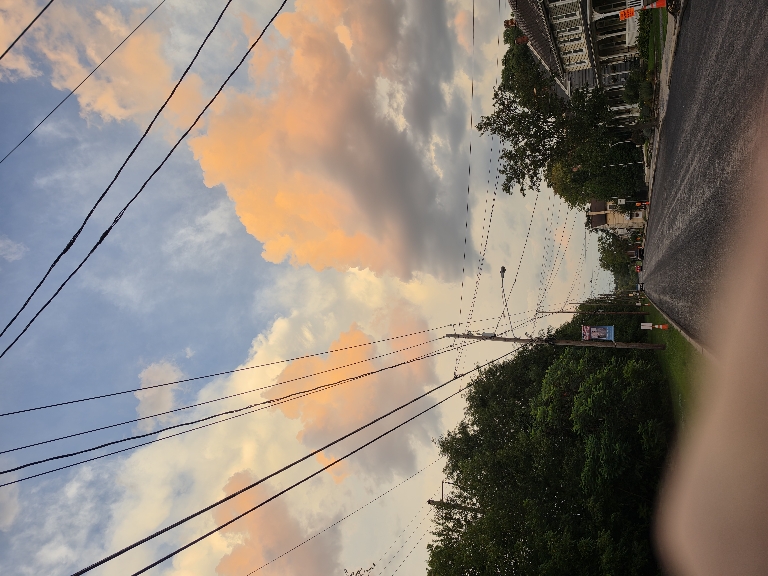 This picture shows bright orange clouds below and in front of of a white thunderstorm to the East.