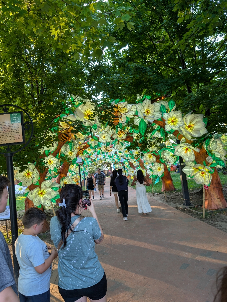 This picture shows a tunnel of lights that show flowers and bees with people in it.