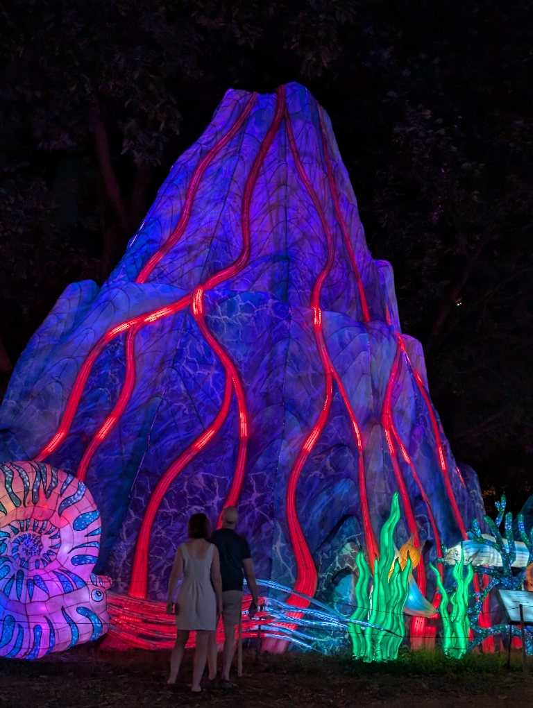 This is a photo of  the large volcano in the dark. The Mountain is lit up bluish gray and has dim red lava coming down the sides.