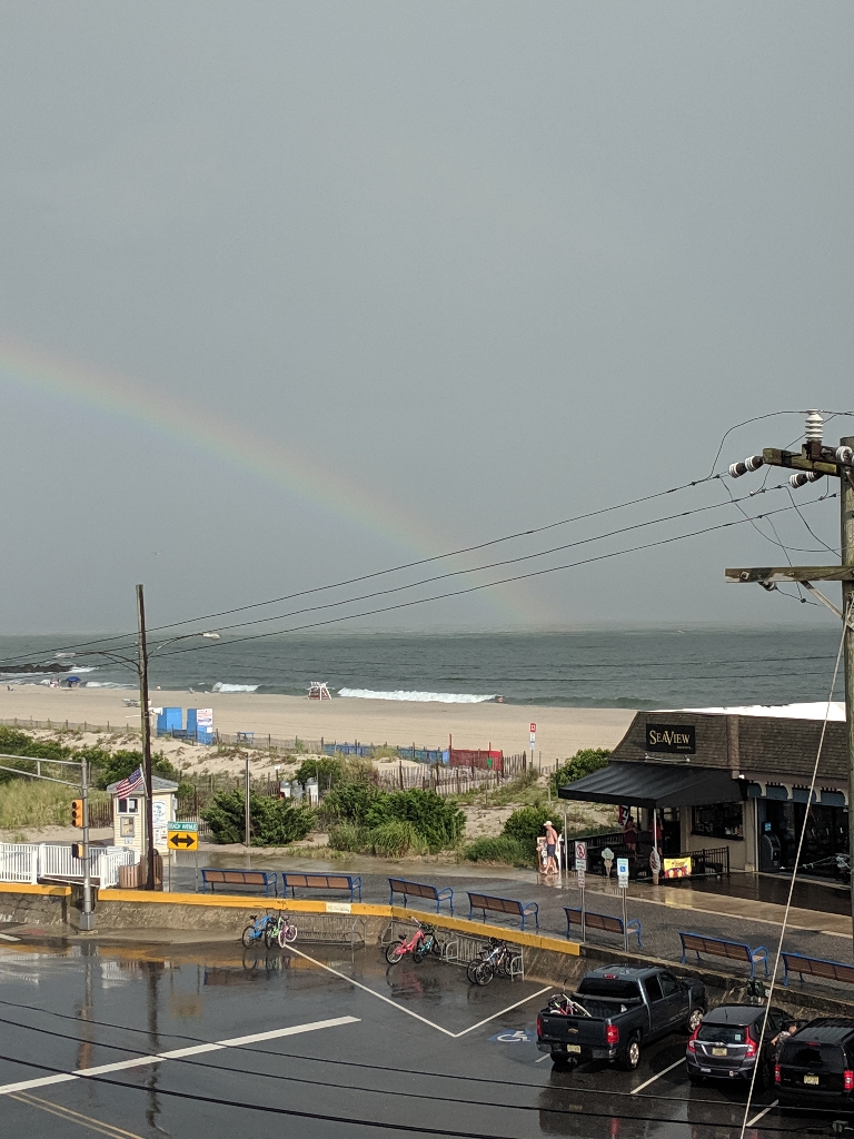 This is a picture of a rainbow over the beach and ocean in Cape may. The departing thunderstorm is in the background