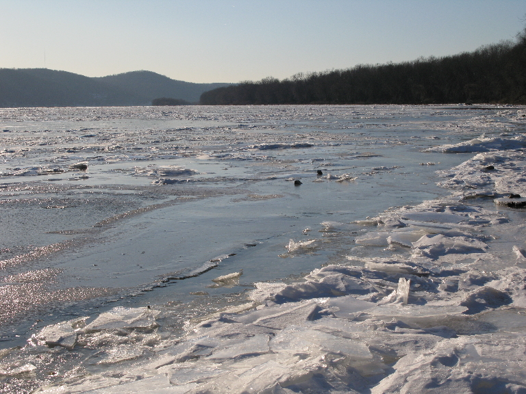 This photo shows a couple of blocks of ice on top of the sheet ice on the river.