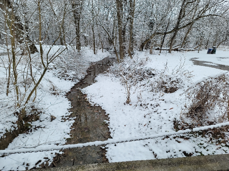 This photo shows a few inches of wet snow surrounding a small stream that is just water.