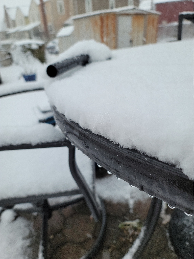This is a picture of a snow covered patio table. There is between one and two inches of snow on the green table