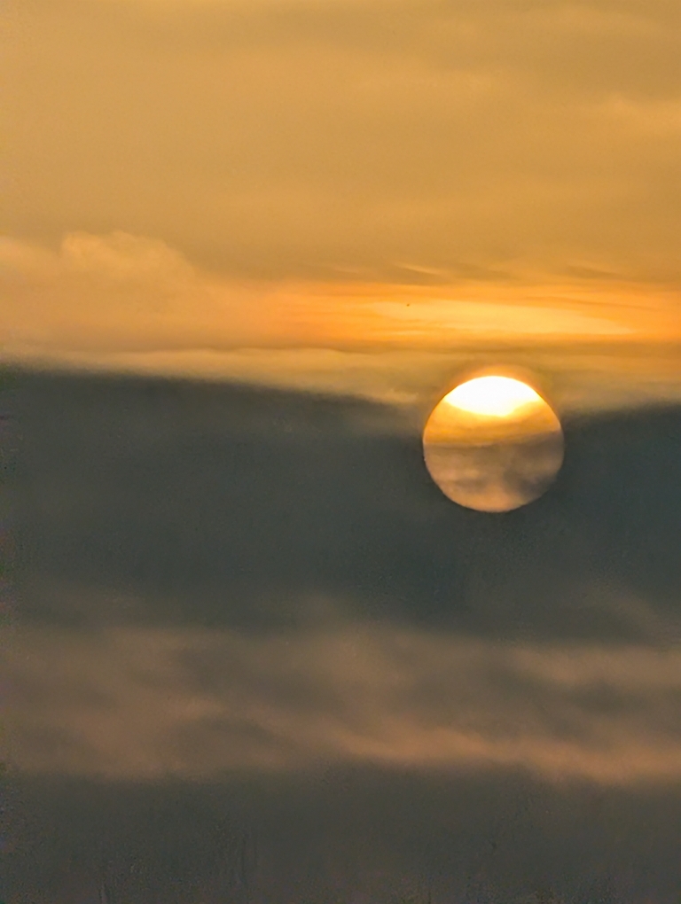 This picture shows a yellow sunrise behind plenty of dark gray clouds