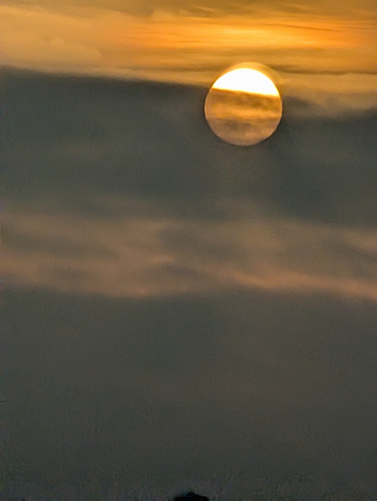 This picture shows a yellow sunrise behind plenty of dark gray clouds