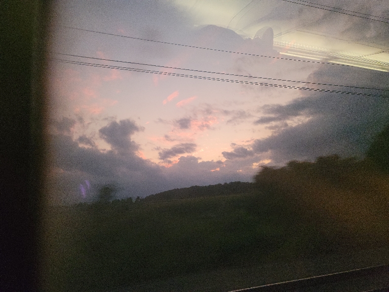 This picture shows somewhat colorful clouds in the sky from a train window. Unfortunately there's also a reflection of the internal lights.