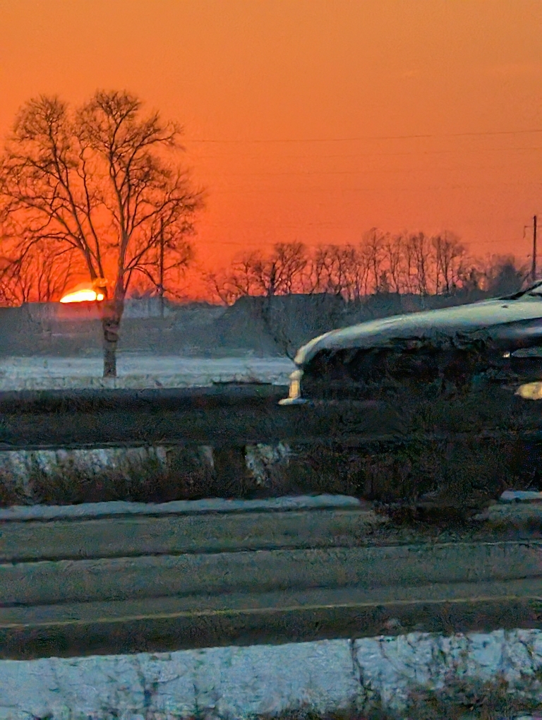 This picture shows a very zoomed-in photo of the very tip of the sun over a snowy field.