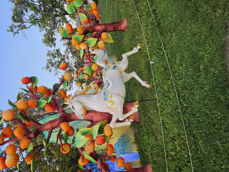 This photo shows an illuminated unicorn with a lit up tree behind it. The lighting isn't real visible due to it still being daylight. 